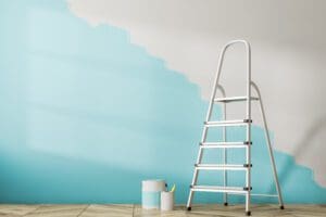 Empty room interior with a wooden floor and a half painted blue wall. A ladder and tins of paint.