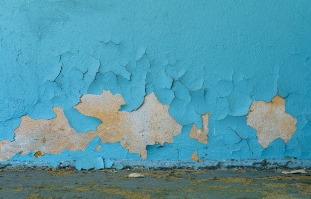 Cracked blue paint on a wall surface with messy ground