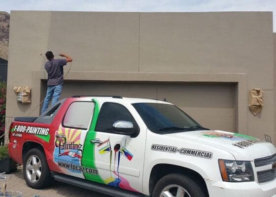 Expertos en Pintura Residencial en los Mercados de Phoenix y Tucson 5 Arizona Painting Company at work: A painter stands on their truck, skillfully painting the residential exterior of a home, showcasing professional expertise and attention to detail.