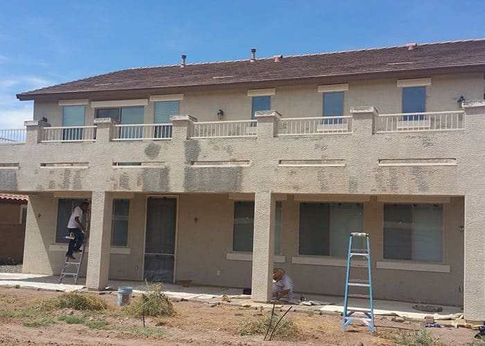 Residential exterior: Brown home in early stages of painting, with painters applying the first coats, signifying a transformation in progress.