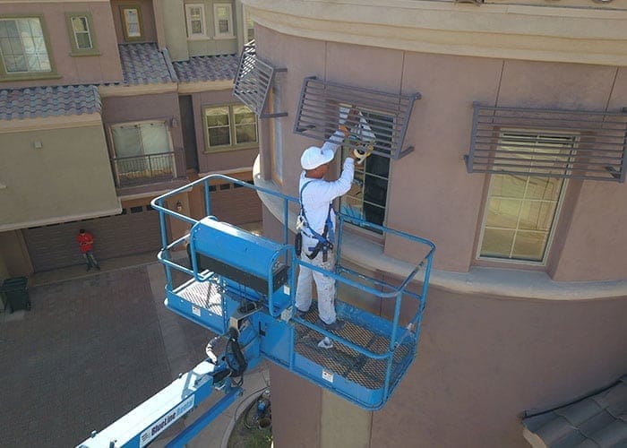 Arizona Painting Company's expert team offering HOA painting services, revitalizing community properties with quality coatings for lasting beauty and enhanced curb appeal. Painter wearing white is shown in the image painting an apartment building as part of HOA painting.