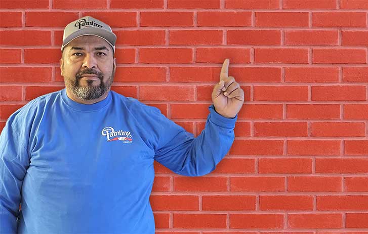 A man from Arizona Painting Company point to a red brick wall